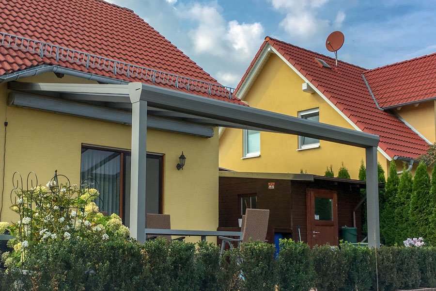 Ein Bild von einem Lounge Bereich unter einem Aluminium Terrassendach mit Glaselementen und Blick in einen schönen Garten.
